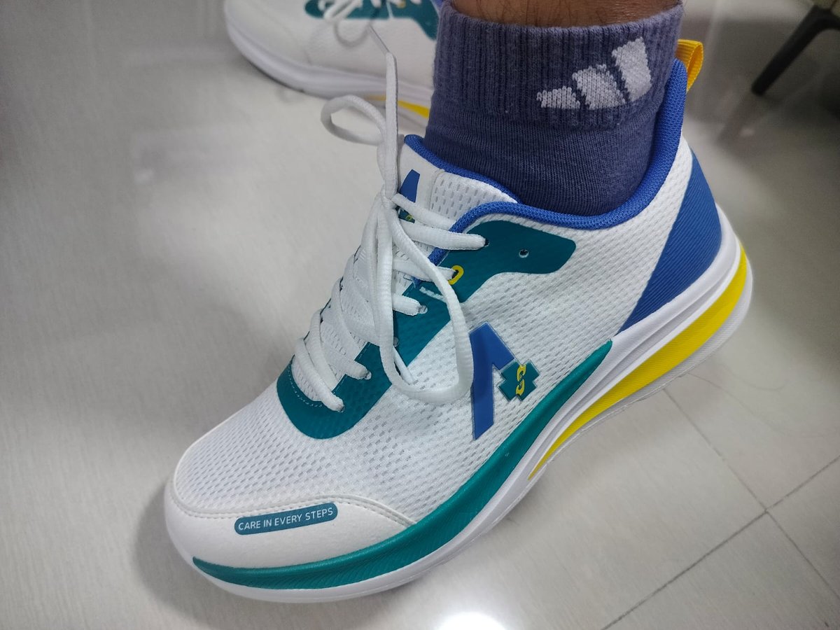 Finished sample shoe worn on a foot, white mesh upper with teal and blue panels, yellow trim along a white midsole