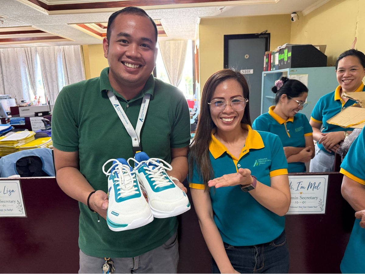 Two staff members at the customer's office smiling and holding up a pair of the finished white and teal shoes